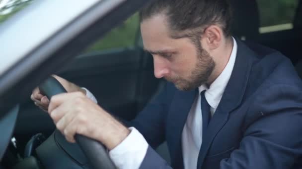 Hopeloze knappe jongeman leunend op het stuur in de auto, schreeuwend. Portret van een blanke man met een baard in pak in een voertuig. Zenuwinzinking en crisisconcept. — Stockvideo