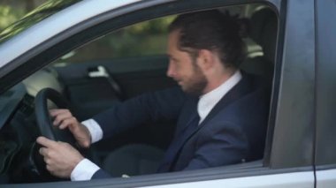 Yandan bakıldığında sinirli erkek, beyaz şoför direksiyona basıp açık havada trafik sıkışıklığında araba kullanıyor. Şoför koltuğunda oturan sinirli adamın portresi..