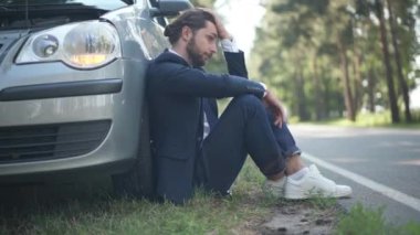 Yan görüş umutsuz genç adam araba arızası ışıkları açık halde banliyö yolundan geçen bir araçla oturuyor. Üzücü, güneşli bir günde beyaz erkek sürücünün dışarıda düşünmesi. Kaza konsepti.