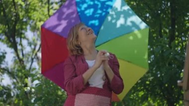 Yavaş çekimde dönen renkli şemsiyeli beyaz bir kadının portresi yukarı bakıyor. Neşeli emekliliğiniz kutlu olsun güneşli bir yaz günü dışarıda eğleniyorsunuz. Yaşlanma ve kendine güven.