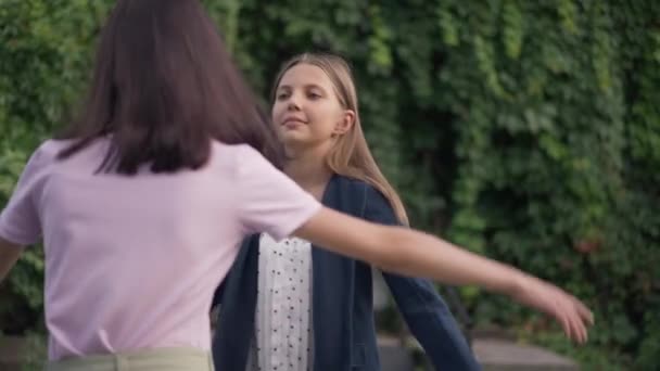 Hypocritical insincere teenage girl hugging friend with annoyed facial expression. Portrait of unhappy Caucasian teenager meeting annoying friend outdoors in park on summer spring day. Slow motion. — Stock Video