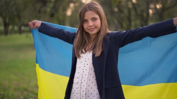 Live kamera zooma in till glada leende tonåring flicka poserar med ukrainska flaggan på våren sommarpark utomhus. Självsäker vit tonåring tittar på kameran leende. Stolthet och patriotism. — Stockvideo