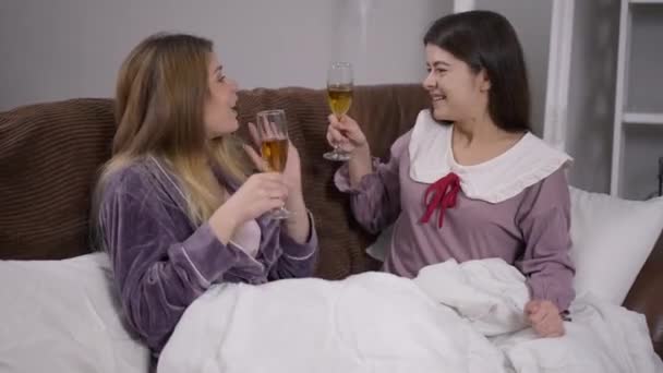 Дві щасливі жінки смажать скло і п'ють вино на вечірці в піжамі. Портрет кавказьких друзів розслаблявся, насолоджуючись відпочинком з алкоголем на вихідних. Концепція дозвілля. — стокове відео