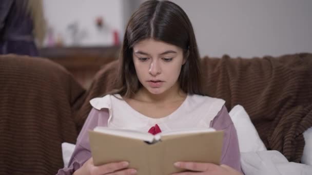 Koltukta oturan, arka planda tanınmayan oda arkadaşıyla kitap okuyan konsantre genç kız öğrenci portresi. Özümsenmiş zeki beyaz kadın ödev çalışıyor.. — Stok video