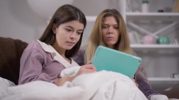 Giovani donne spaventate con espressione facciale spaventata che guardano film horror online su tablet al pigiama party. Ritratto di amici caucasici appoggiati sul divano scioccati dal film. — Video Stock