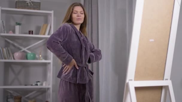 Selvsikker smuk ung kvinde i pyjamas beundrer refleksion i spejlet bliver smilende. Portræt af kaukasiske narcissist ved sengetid hjemme indendørs. Selvtillid og skønhed koncept. – Stock-video