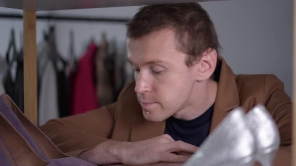 Imagen de un hombre gay inseguro dudando en elegir zapatos en la tienda en el interior y posando mirando a la cámara. Retrato de cerca de una persona LGBT caucásica pensando en comprar tacones altos. Movimiento lento. — Vídeos de Stock