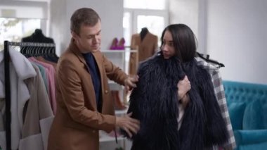 Beyaz eşcinsel bir adam dükkanda kürk seçen bir kadına yardım ediyor. LGBT 'den memnun bir kişinin portresi güzel bir bayana Kara Cuma satışları için yeni kıyafetler almasını tavsiye ediyor. Yavaş çekim.