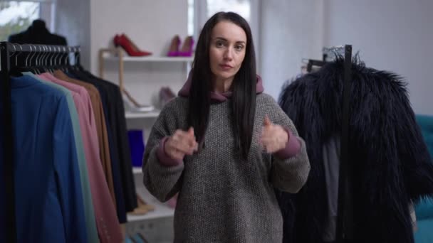 Портрет упевненої Кавказької вродливої жінки, що намагається одягнути великий светр з капюшоном у майстерні моди. На перший погляд дбайливий покупець вибирає новий одяг у повільному русі.. — стокове відео