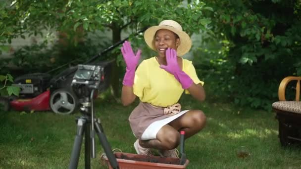 Mujer afroamericana positiva saludando hablando grabando video blog agrícola en cámara al aire libre. Retrato de joven jardinero confiado hablando en cámara lenta sonriendo plantando semillas en maceta. — Vídeo de stock