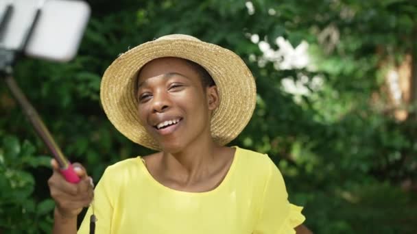 Portré elégedett afro-amerikai nő szalmakalapos csinál szelfi áll a kertben a szabadban a napos nyári tavaszi napon. Boldog magabiztos fiatal karcsú hölgy élvezi hétvégén szabadban. — Stock videók