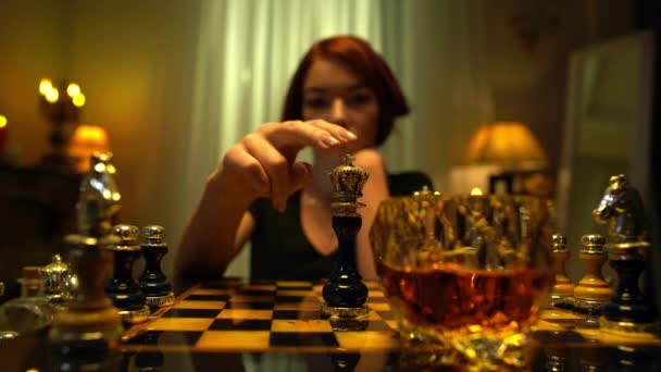 Chess king knocked down by female slim hand with blurred redhead woman putting chin on hands at background. Professional player winning in game indoors with serious facial expression. — Stock Video