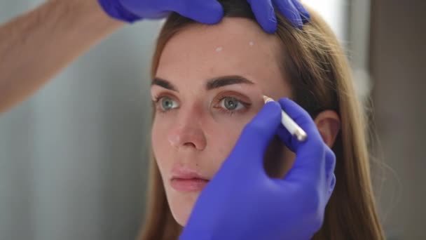Detailní záběr rukou v rukavicích označujících tečky pro kosmetické injekce na ženskou tvář. Nerozpoznatelný kavkazský kosmetik připravuje klienta na vstřikování faceliftových výplní. Koncept ženskosti a péče o krásu. — Stock video