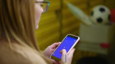 İçeride dövmeli genç kadın elleri olan mavi ekranlı akıllı telefon. İnternette gezinen bulanık beyaz kadın telefon uygulaması kullanarak sarı depo deposunda duruyor..