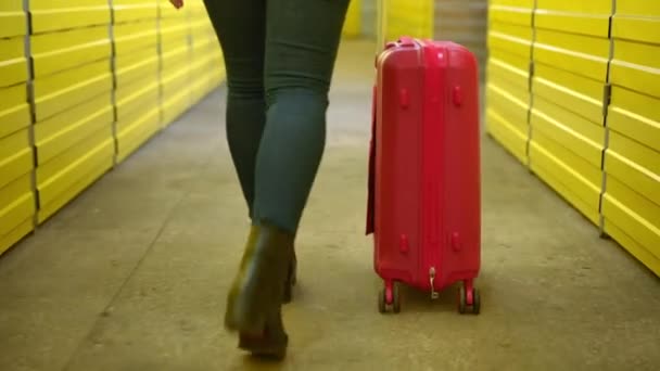 Vista posteriore gambe di giovane donna passeggiando con bagaglio a mano rosso in magazzino giallo. Donna caucasica irriconoscibile che cammina con la valigia in magazzino. Tracking shot, telecamera in diretta. — Video Stock