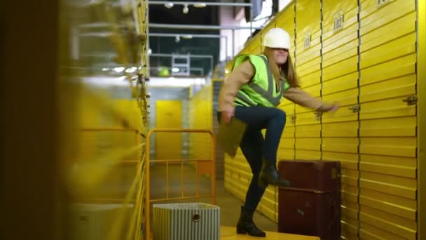 Bred skott glada glad kvinna dansar på industriell vagn i gult lager inomhus. Glada kvinnliga kaukasiska anställd har roligt glädje inomhus i lager. Lycka och livsstil koncept. — Stockvideo