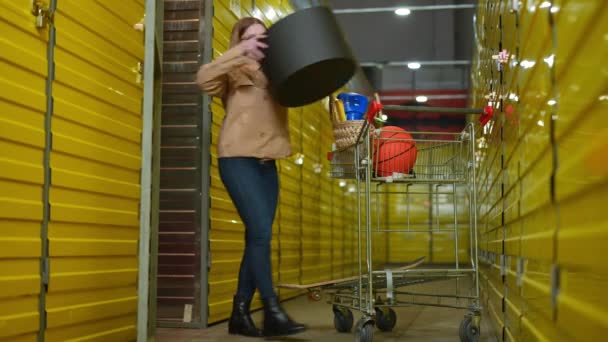 Een wijdverspreide jonge vrouw die spullen opslaat in de opslagruimte in gele zelfopslag. Portret van een blanke huurder in een pakhuis binnenshuis. — Stockvideo