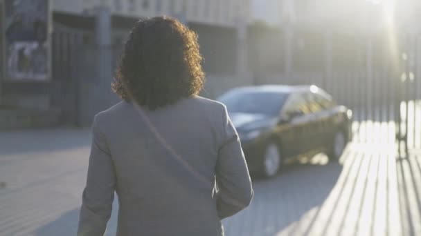 Voltar ver o homem de terno com cabelos longos andando para carro luxuoso preto na cidade. Rastreamento tiro de empresário caucasiano confiante passeando até o veículo em raios de sol ao ar livre. Câmara lenta, câmara ao vivo. — Vídeo de Stock