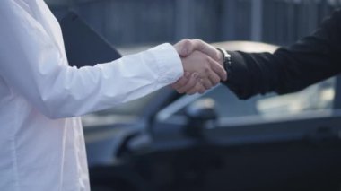 Şehir caddesinde siyah arabanın önünde beyaz erkek ve kadın tokalaşması. Tanınmayan iş ortakları yavaş çekimde el sıkışıyor. İşbirliği ve ortaklık kavramı.