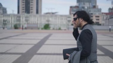 Canlı kamera, şehir meydanında ağır çekimde yürüyen adamı izliyor. Kafkasyalı genç işadamının şehir merkezinde gezintiye çıkışının yan görüntüsü. İş hayatı.
