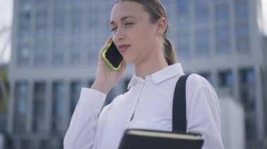 Başarılı, pozitif, güzel bir kadın telefonda konuşuyor ve gülümsüyor. Kafkasyalı mutlu genç iş kadınının portresi gökdelende iş birliğini tartışıyor ağır çekimde..
