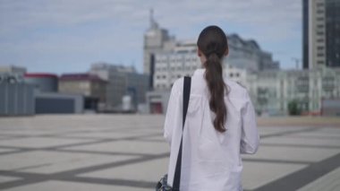 Şehir meydanında ağır çekimde yürüyen zayıf, beyaz bir kadın. Kendine güvenen zarif iş kadınının şehir merkezinde gezinirken çekilen görüntüsü. İş hayatı konsepti.