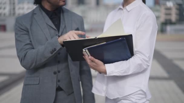 Onherkenbare man en vrouw bespreken zaken die buiten op het stadsplein staan. Kaukasische mannelijke en vrouwelijke partners praten in slow motion over het analyseren van project strategie idee. — Stockvideo