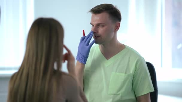 Porträtt av självsäker professionell plastikkirurg som förklarar näsplastik för klienten i medicinsk klinik. Positiv expert kaukasisk man talar med kvinna vidrör näsan undersöka patienten. — Stockvideo