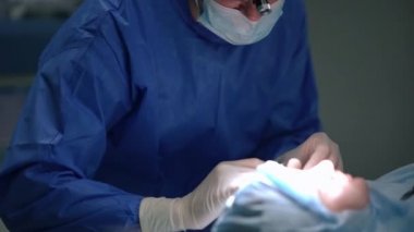 Konsantre cerrah ameliyat yatağında yatan hastanın yüzünü inceliyor. Tıbbi klinikte ağır çekimde ameliyat yapan uzman bir doktorun portresi..