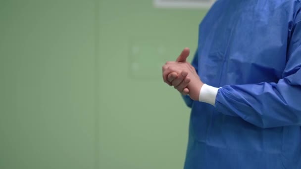 Неузнаваемый белый мужчина в хирургическом халате, растирающий руки в замедленной съемке, стоя справа в операционной. Профессиональный хирург-эксперт готовится к инвазивной операции в помещении. — стоковое видео