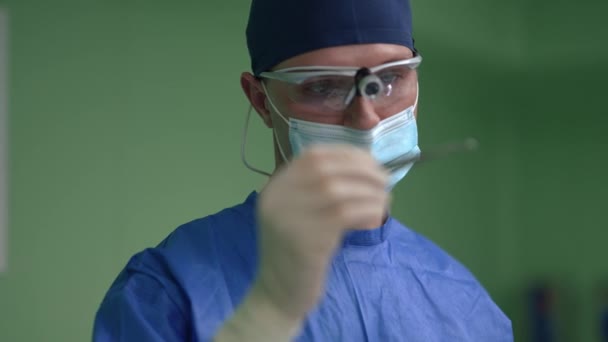 スローモーションでメスを調べる重度の集中男性外科医の肖像。屋内病院の手術室に立つ制服や外科マスクの白人専門家の男。医学の概念. — ストック動画