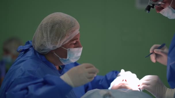 Kaukasisk sjuksköterska och kirurg som opererar ögonlocken på kliniken inomhus. Självsäker koncentrerad man och kvinna som opererar i operationsrummet för patienten. Långsamma rörelser. — Stockvideo