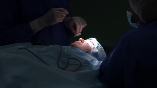 Plastisch chirurg controleert penmarkering dissectie op ooglid van jonge vrouw liggend op chirurgische bed. Blanke deskundige arts opererende patiënt in slow motion. Esthetische chirurgie en gezondheidszorg. — Stockvideo