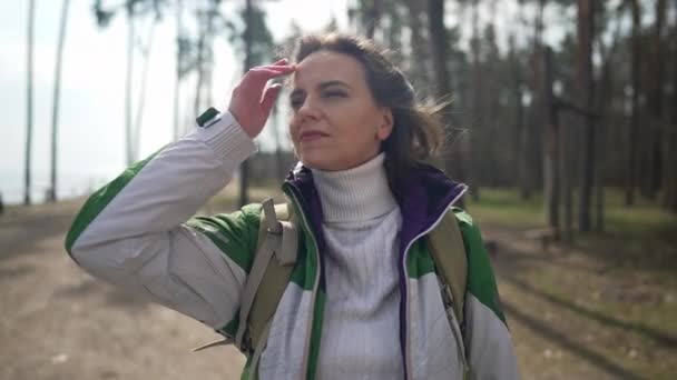 Positiva encantadora mujer caucásica de pie en el claro del bosque admirando la belleza de la naturaleza y mirando a la cámara sonriendo. Feliz turista femenina posando en cámara lenta en el día de otoño primavera en el bosque. — Vídeos de Stock