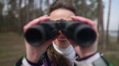 Dürbün kullanan gülümseyen kadın ormanda kameraya bakıyor. Kafkasyalı turistin dışarı çıkıp tatilin tadını çıkardığından emin olmak güzel. Yavaş çekim.