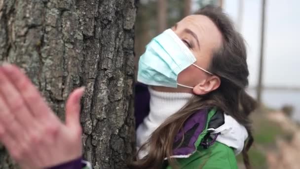 Aantrekkelijke vrouw in Covid gezicht masker knuffelen boomstam staan in de herfst lente bos buiten. Portret van blanke vrouwelijke reiziger genieten van vrije tijd bewonderen van de natuur in slow motion. — Stockvideo