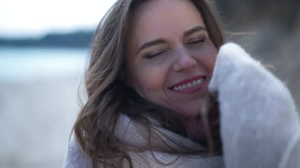 Coqueta hermosa mujer cerrando la cara inferior con manta mirando a la cámara sonriendo. Retrato de la dama caucásica coqueteando posando en cámara lenta al aire libre en la orilla del río. — Vídeos de Stock