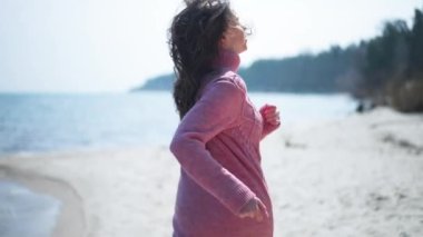 Arkaya bakan güzel, korkmuş kadın ağır çekimde geriye doğru koşuyor. Pembe örgü elbiseli korkmuş beyaz kadın kumlu sahilde güneşin altında tehlikeden kaçıyor. Panik ve korku.