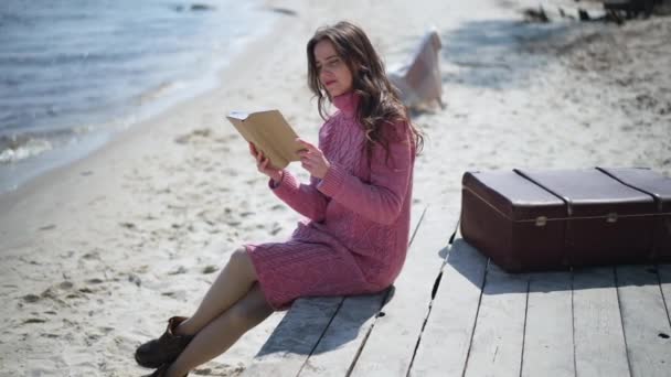 Ampio colpo assorbito donna caucasica lettura libro seduto sul molo di legno sulla spiaggia di sabbia. Fidato lettore femminile intelligente godendo hobby sulla calma giornata di sole all'aperto. Rallentatore. — Video Stock