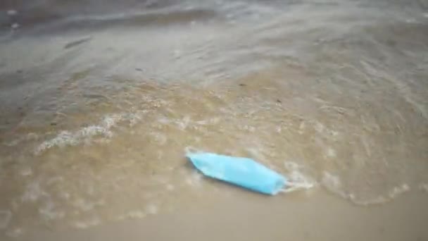 Live-Kamera begleitet Coronavirus Gesichtsmaske schwimmen in Wellen rollen auf Sandstrand. Müll am Meeresufer der Covid-19-Pandemie. Umweltschäden und Umweltverschmutzung. — Stockvideo
