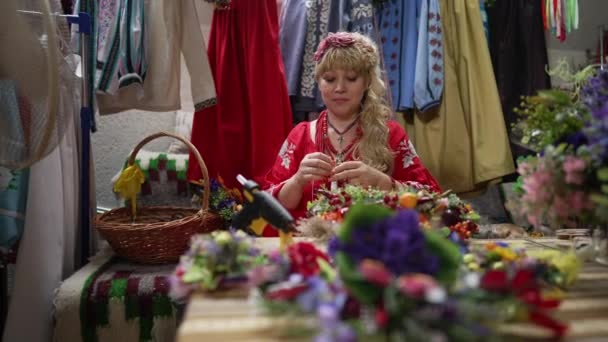 Yapıştırıcı kullanan pozitif kadın portresi el sanatları atölyesinde geleneksel Ukrayna aksesuarları yapıyor. Kendine güvenen zanaatkar gülümsüyor. Masada oturuyor ve ağır çekimde baş çelengi yapıyor.. — Stok video