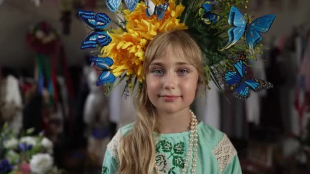 Detailní portrét okouzlující ukrajinské holčičky dívající se na usmívající se kameru. Krásné dítě v národních vyšívaných šatech a věnec s hlavou pózující ve zpomaleném filmu uvnitř. Státní příslušnost a individualita. — Stock video