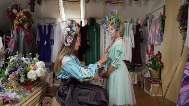 Side view όμορφο κορίτσι στην παραδοσιακή ουκρανική κεντημένο φόρεμα στέκεται σε εσωτερικούς χώρους ως αδελφή προσαρμογή εθνική φορεσιά σε αργή κίνηση. Χαμογελαστό χαρούμενο παιδί με αδερφό μέσα. Οικογένεια και χαρά. — Αρχείο Βίντεο