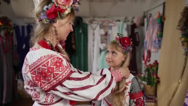 Mujer ucraniana sonriente acariciando el pelo largo de la chica feliz en el vestido bordado tradicional. Hermosa joven madre hablando con encantadora hija en el interior en cámara lenta. Concepto familiar. — Vídeos de Stock