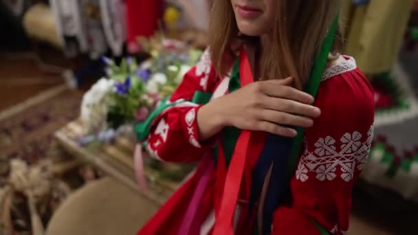 Mujer joven ucraniana irreconocible acariciando cintas de colores sentados en el interior en traje nacional. Señora delgada de confianza en vestido rojo bordado sonriendo. Movimiento lento. — Vídeo de stock