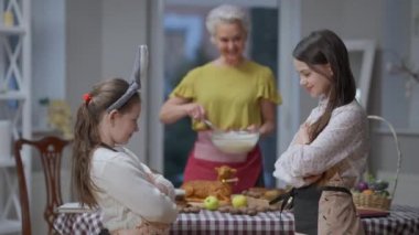 Tartışmalı kız kardeşler barış için el kol hareketi yapıyor evde sarılıyorlar. Arka planda Paskalya yemeği pişiren bulanık gülümseyen büyükanne. Aile ve mutluluk kavramı.