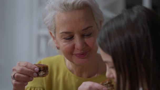 Close-up mujer positiva degustación de delicioso postre de Pascua con chica adolescente en el interior. Retrato de la feliz abuela caucásica hablando con su nieta disfrutando de la comida. — Vídeos de Stock