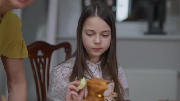 Adolescente mangeant le dessert de Pâques comme grand-mère cuisinant et petite sœur passant à l'arrière-plan. Portrait de belle fille caucasienne appréciant gâteau d'agneau doux savoureux regardant autour. — Video