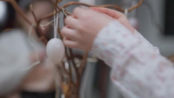 Девушка руки висит цветные пасхальные яйца в помещении с размытой семьи на заднем плане. Неузнаваемый кавказский подросток украшает дом в праздник. — стоковое видео