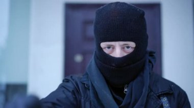 Evin arka planında duran kameraya bakan maskeli adamın yakın plan portresi. Tehlikeli şüpheli erkek hırsız dışarıda el kol hareketi yapıyor. Soygun riski ve suç kavramı.